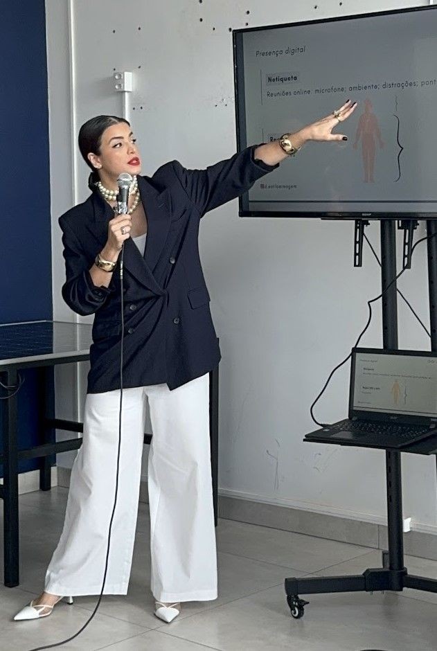 Woman in formal attire holding a microphone and pointing to a screen during a presentation.