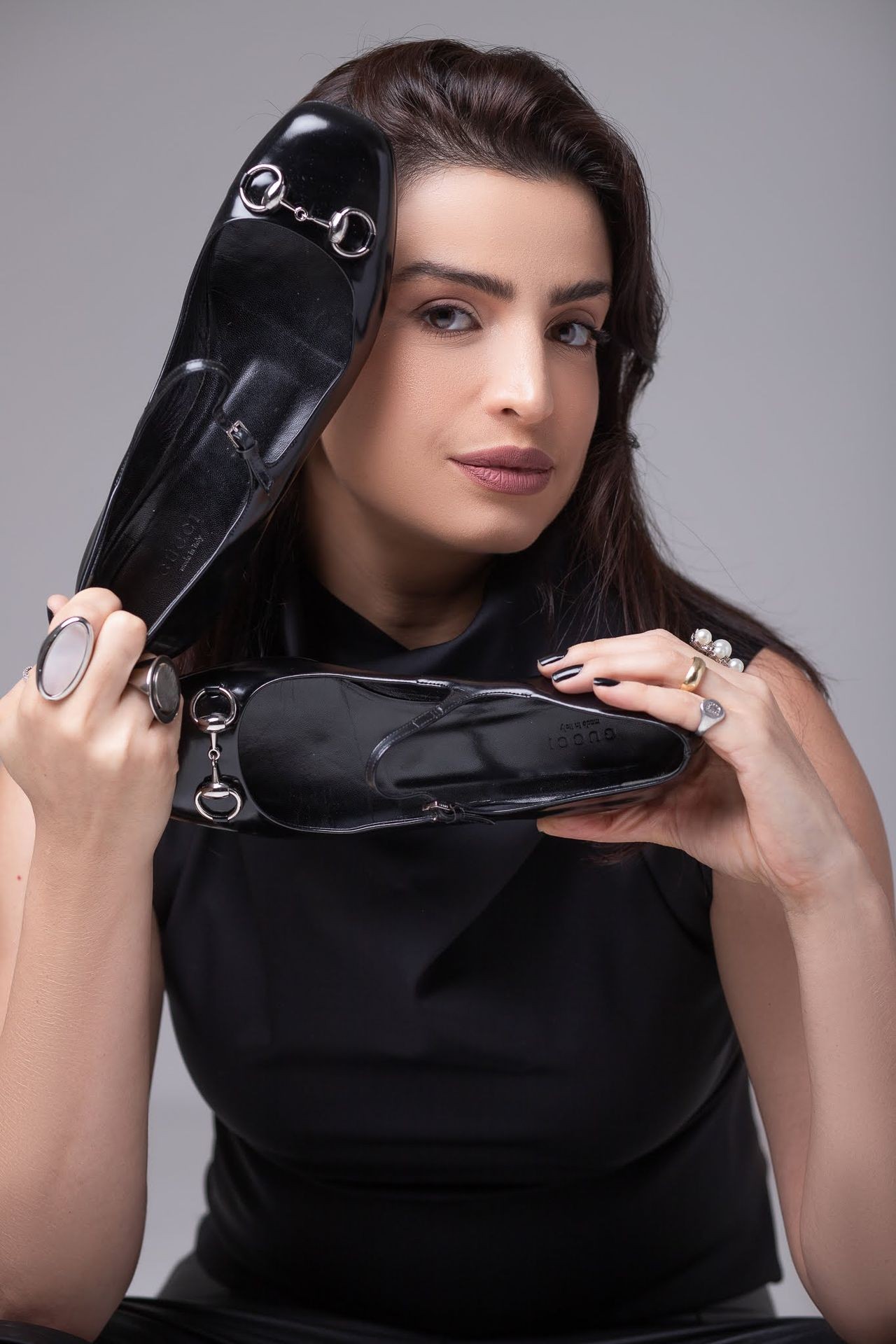 Person wearing rings on both hands holding up a pair of black leather loafers with silver hardware.